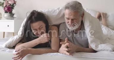 积极的高加索夫妇躺在毯子下的床上，聊天和<strong>大笑</strong>。 微笑着成熟的<strong>男人</strong>
